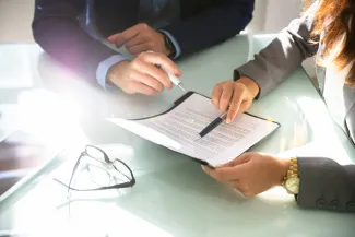 Two Businesspeople Analyzing Document Over Glass Desk