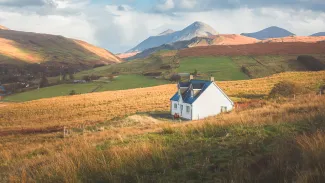 A lone traditional Scottish Highlands white croft house cottage in a rural mountain landscape countryside with Glamaig Peak and the Red Cuillins on the Isle of Skye Scotland