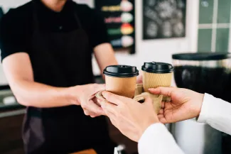 Worker handing takeaway disposable coffee cups to customer