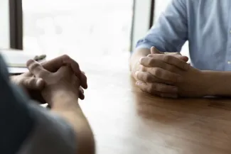 Two men on opposite sides of table with hands clasped