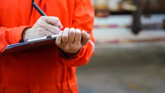 Safety officer man in hi-vis writing on clipboard