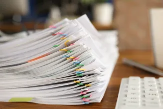 Stack of paperwork held together by colourful paper clips next to calculator