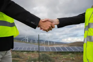 People shaking hands in front of solar and turbine field