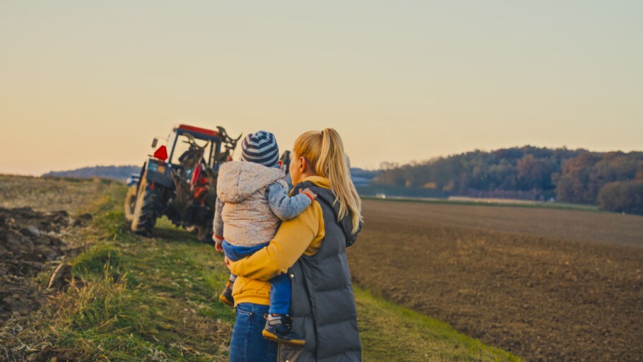 blonde-haired mother and her young son observe a red tractor working