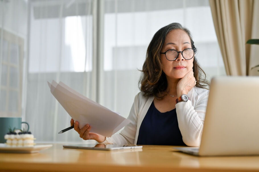 Older woman working at laptop with papers in hand