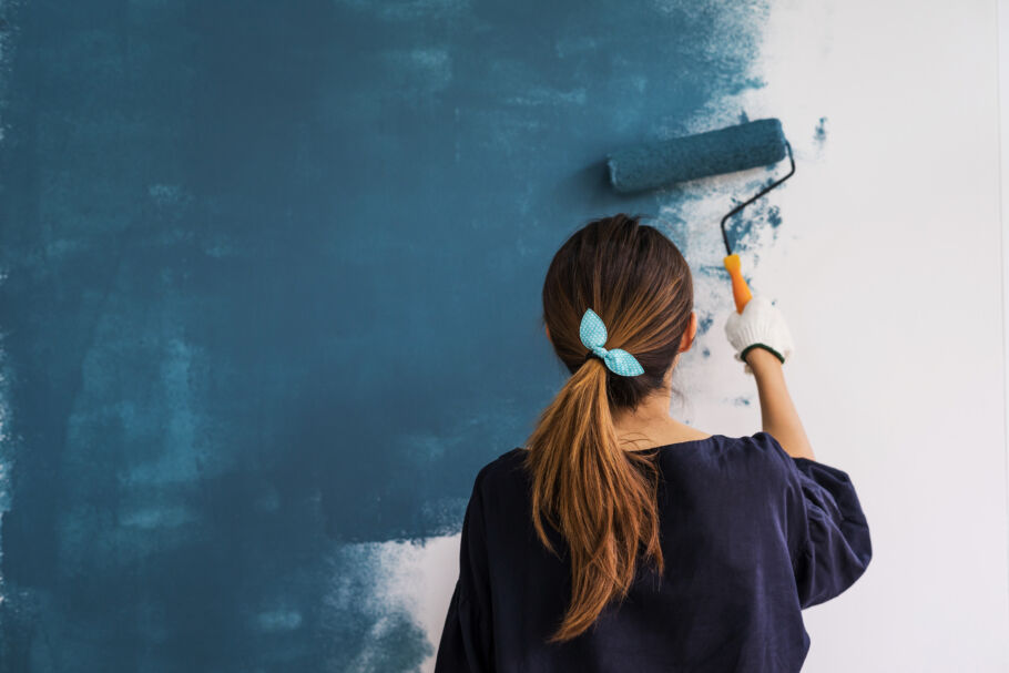Young happy Asian woman painting interior wall with paint roller in new house