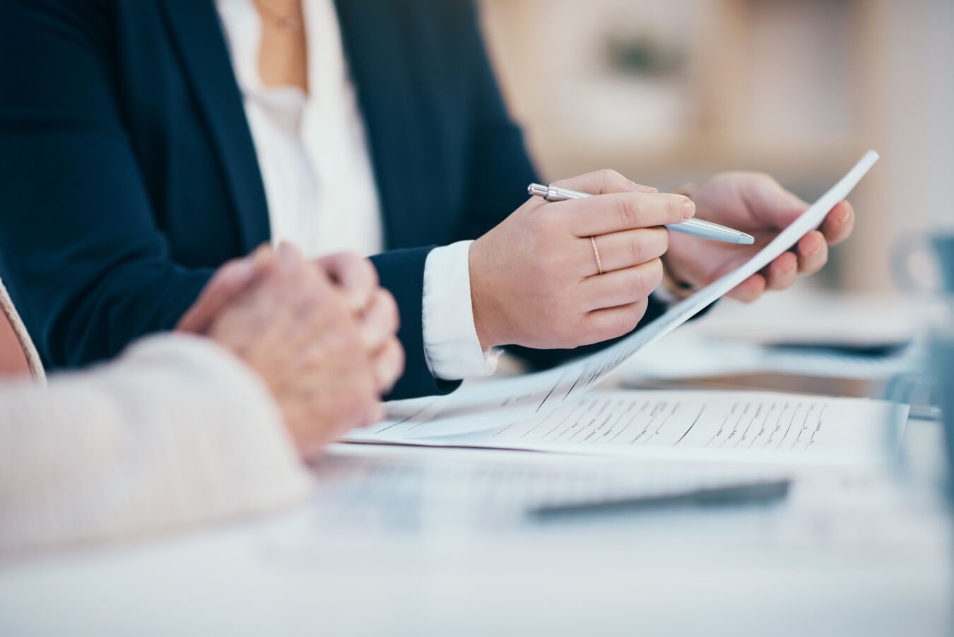 Woman holding pen and pointing at paperwork while other person listens