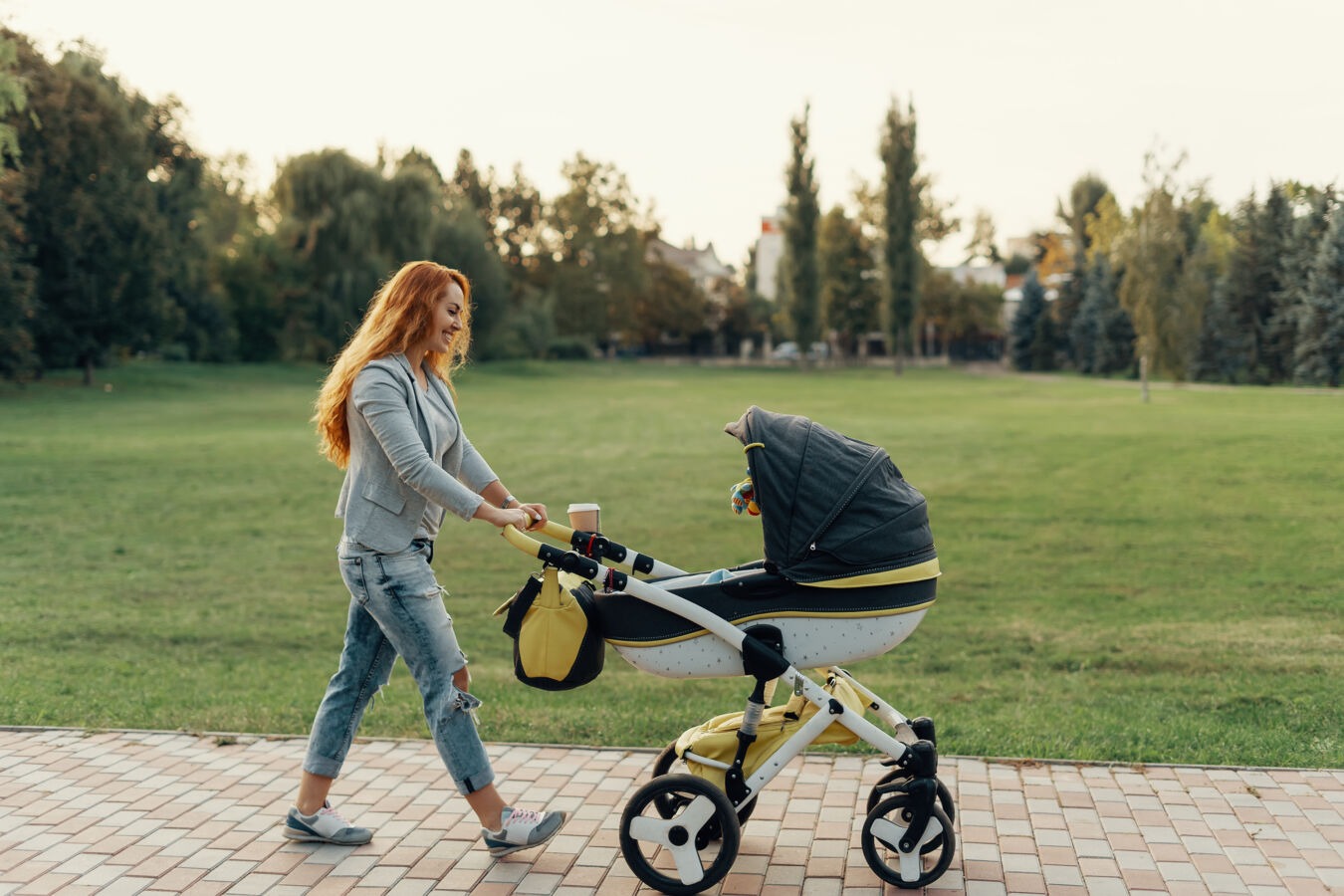 Mother pushing baby in pram through a park