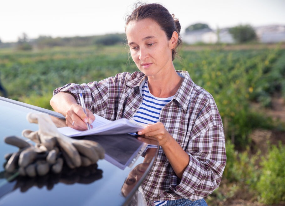 Young woman farmer signing paperwork on truck at farm