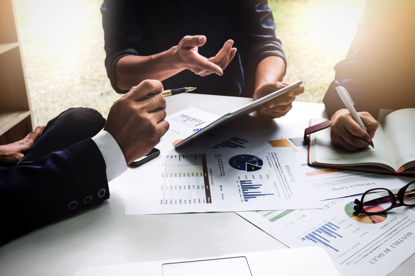 employees having a meeting at a desk with financial documents and an ipad