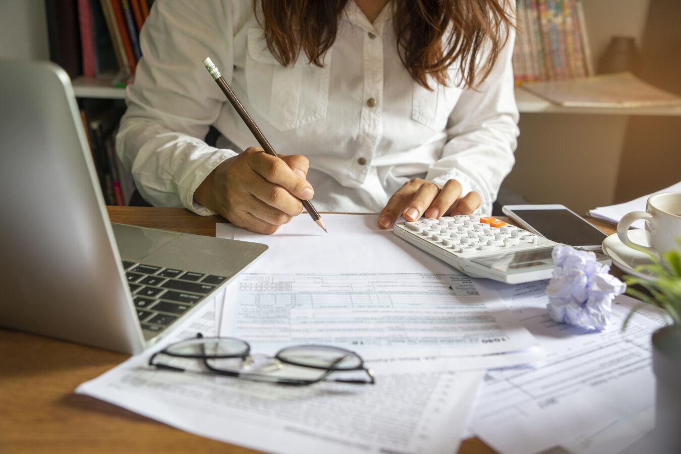 Woman with pen in hand looking over paperwork with calculator
